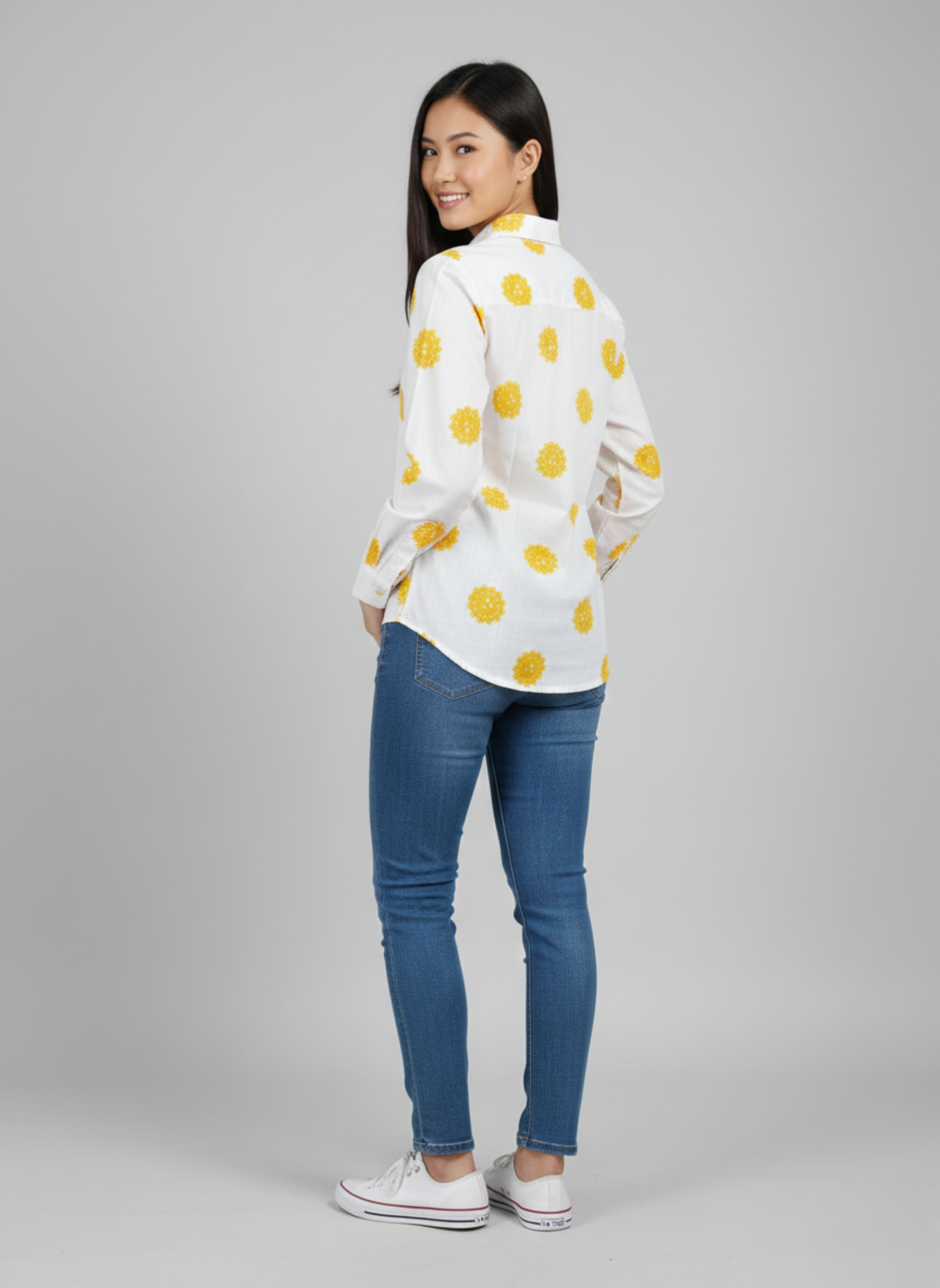 gray parrot shirt Woman wearing a white blouse with yellow polka dots and blue jeans on a gray background